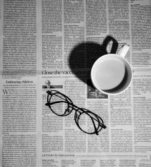 a cup of coffee and a pair of glasses on a newspaper by Ashni courtesy of Unsplash.