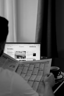 a man sitting at a desk reading a newspaper by Anna Keibalo courtesy of Unsplash.
