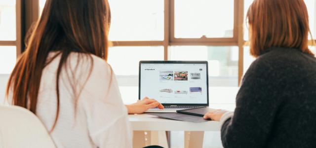 two women talking while looking at laptop computer by KOBU Agency courtesy of Unsplash.