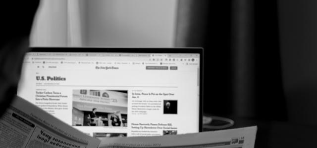 a man sitting at a desk reading a newspaper by Anna Keibalo courtesy of Unsplash.